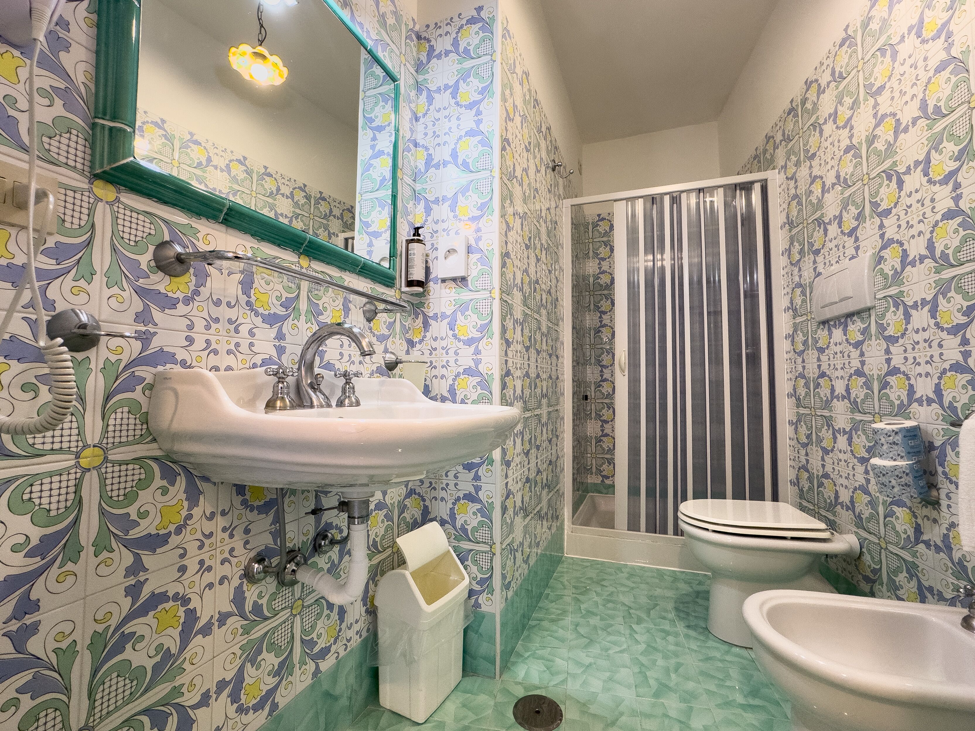 Une salle de bain équipée d’un lavabo, de toilettes, d’un bidet, d’un rideau de douche et de carreaux décorés.