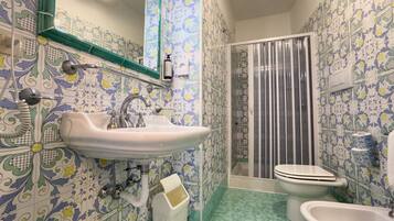 Une salle de bain équipée d’un lavabo, de toilettes, d’un bidet, d’un rideau de douche et de carreaux décorés.
