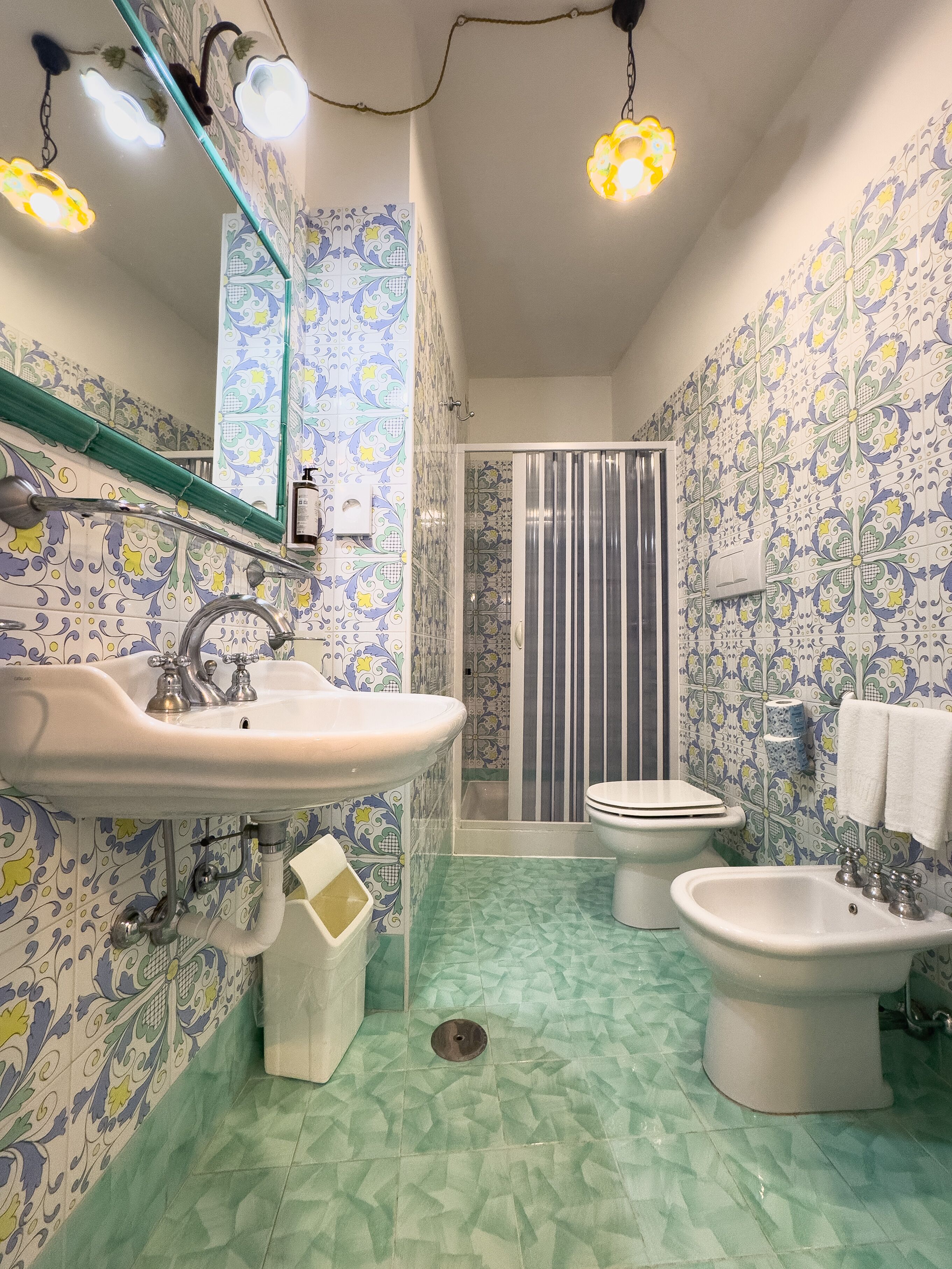 A bathroom with patterned tiles, a sink, bidet, toilet, shower, and hanging lights.