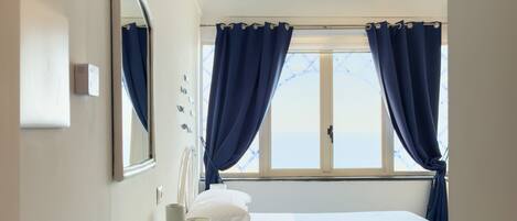 Un dormitorio con cama, mesita de noche, espejo, ventana con cortinas y una lámpara en el techo.