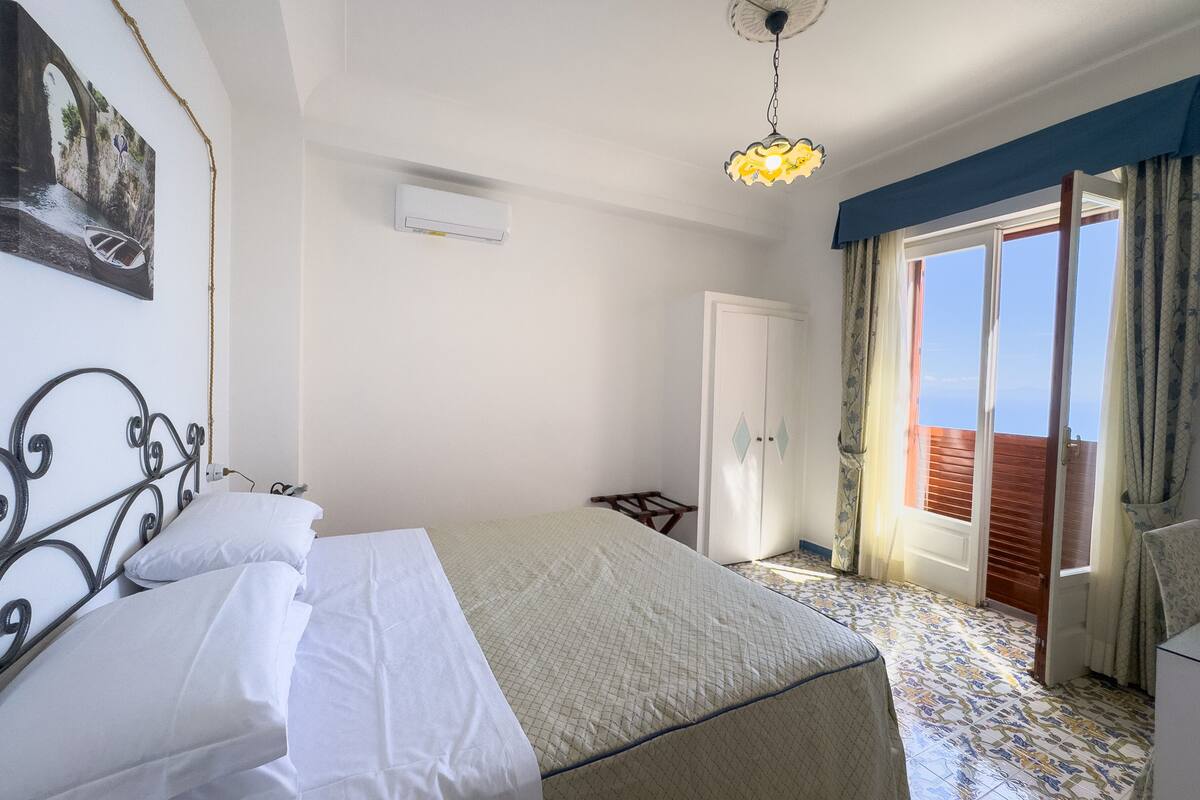 A bedroom with a bed, a wardrobe, a door leading to a balcony, and a ceiling light fixture.