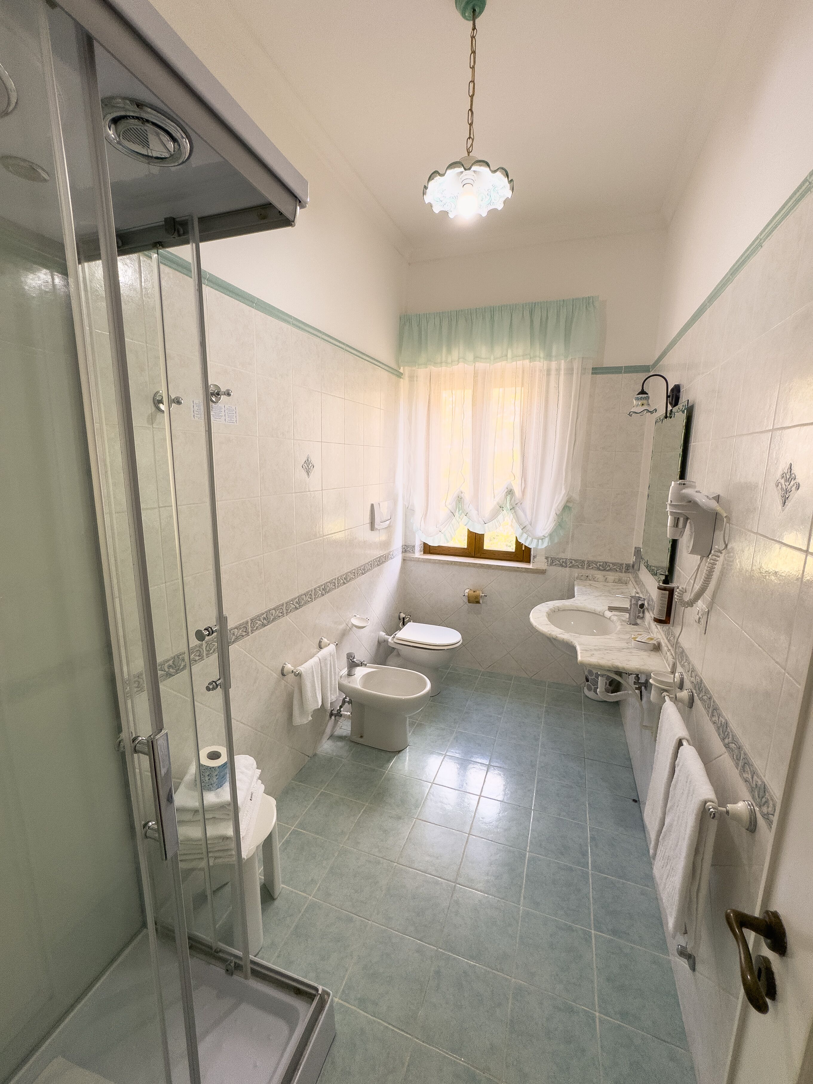 Un baño con cabina de ducha de vidrio, dos inodoros, un bidé, un lavabo y un espejo.