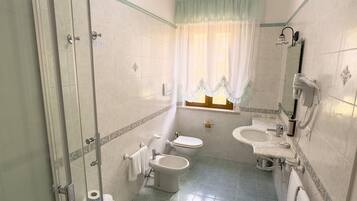 Un baño con cabina de ducha de vidrio, dos inodoros, un bidé, un lavabo y un espejo.
