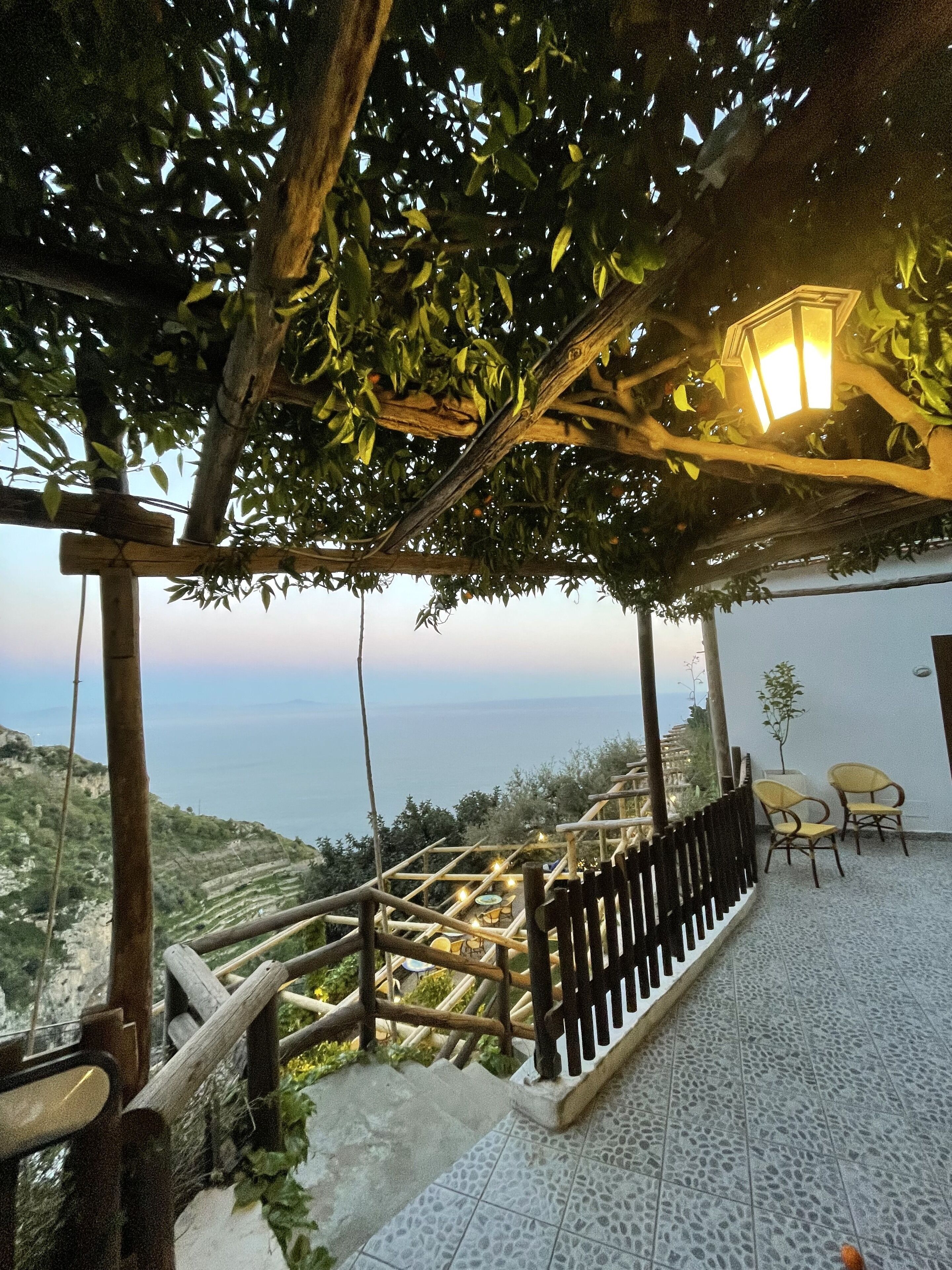 A terrace with a view of the sea, wooden railings, and outdoor seating.
