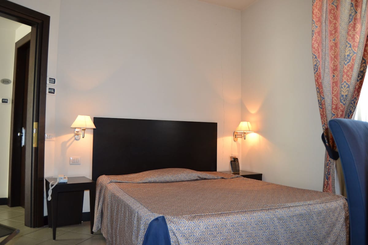 A hotel room with a bed, bedside tables, lamps, and a chair.