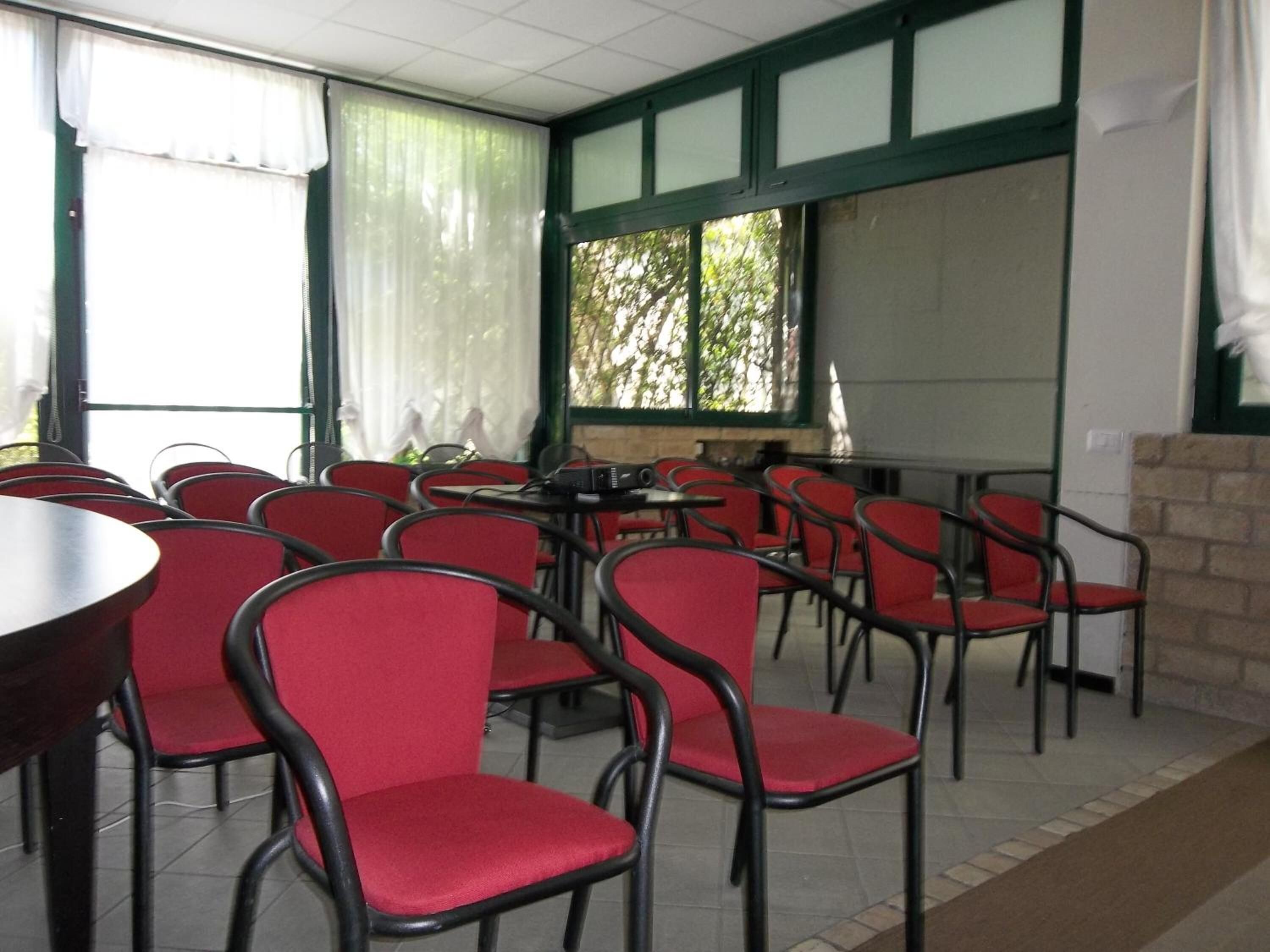 Una habitación con sillas y mesas rojas, ventanas amplias con cortinas y una chimenea de ladrillo.