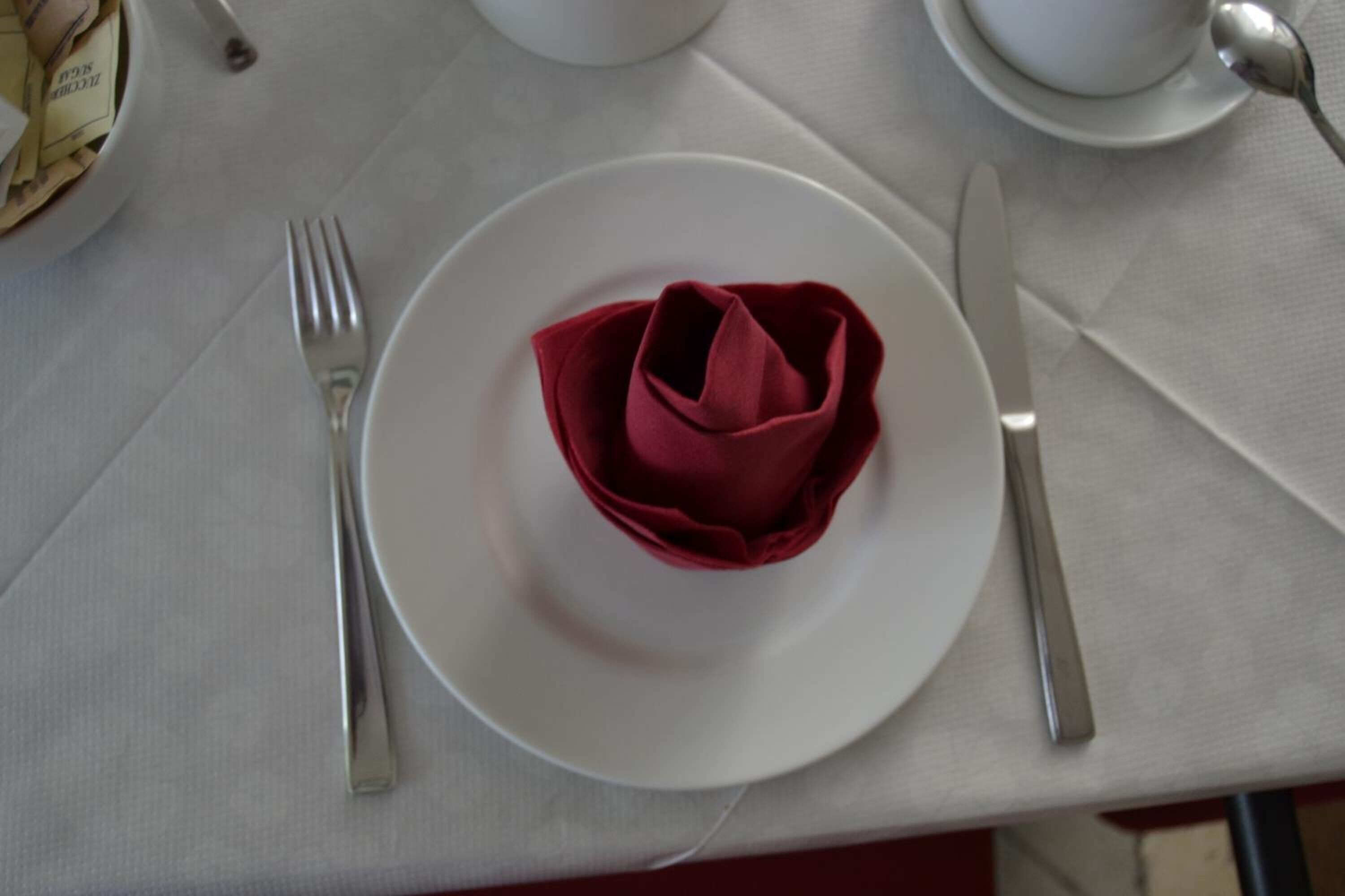 Ein Tisch mit weißer Tischdecke, ein Teller mit einer roten Rose, eine Gabel, ein Messer und ein Löffel.