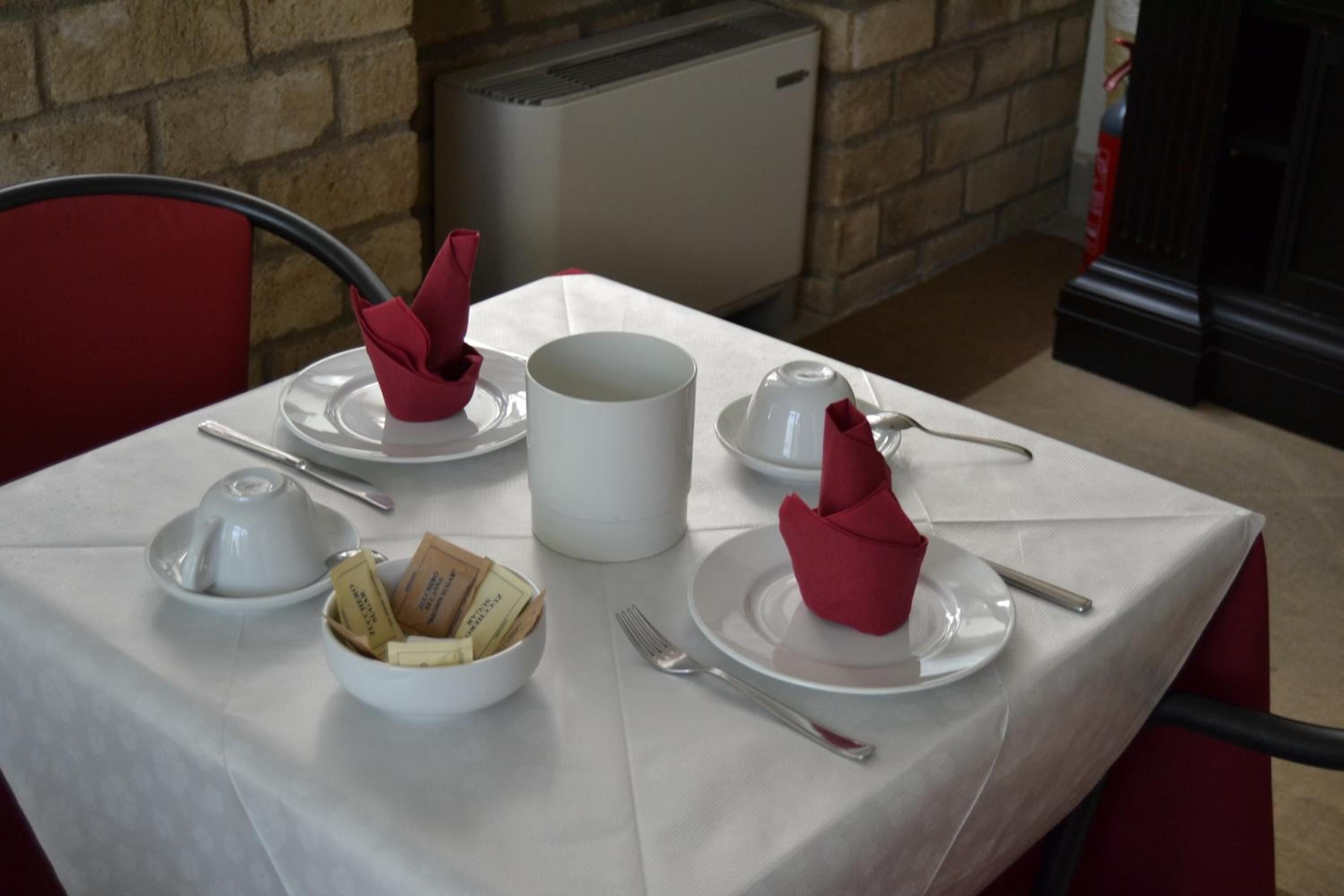 Mesa dispuesta para dos personas, con mantel blanco, servilletas rojas y un tazón de bombones.