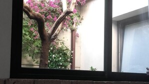 Ett bord dukat för två personer med vita dukar och röda servetter, en vit kopp och en vit skål. Genom ett fönster syns ett träd med rosa blommor och en byggnad i bakgrunden.