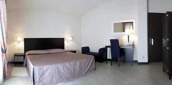 A hotel room with a bed, a desk, a chair, and a wardrobe.