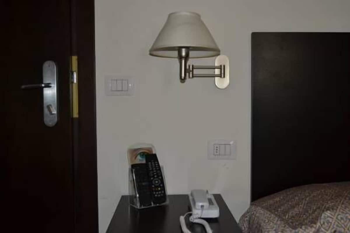 A hotel room with a bed, a bedside table with a lamp, a telephone, and a remote control.