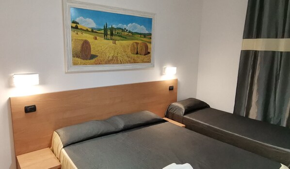 Habitación de hotel con dos camas, un cuadro de un paisaje rural y una luz nocturna.