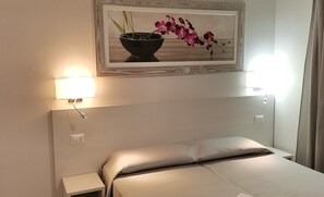 A hotel room with a bed, a nightstand, a wall-mounted lamp, and a framed picture of flowers. - Angelica (Rome)