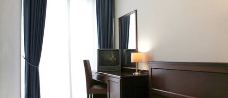 Een hotelkamer met een bed, een bureau met een televisie, een stoel, een lamp en een raam met gordijnen.