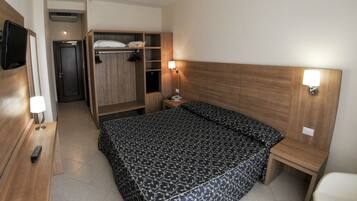 A hotel room with a bed, a wooden wardrobe, a bedside table with a lamp, and a television mounted on the wall.
