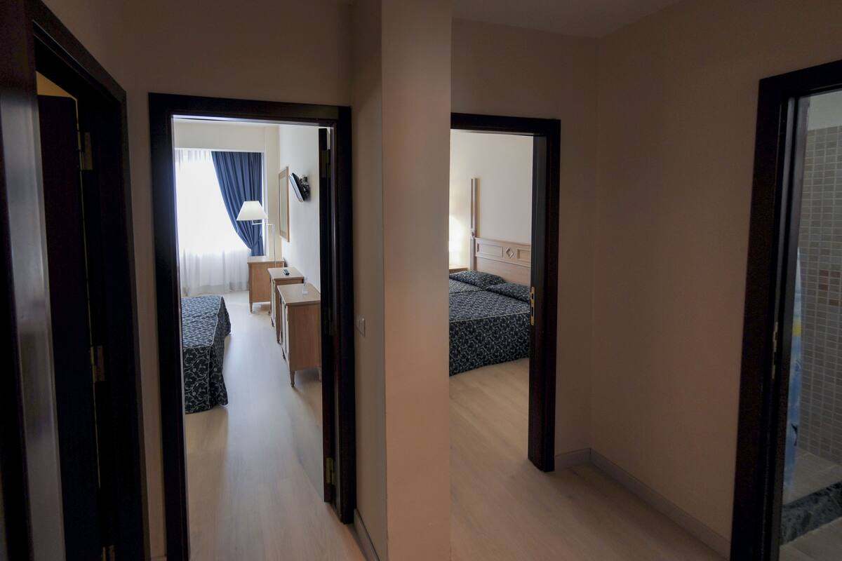 A hotel corridor with a bed, bedside table, and a mirror.
