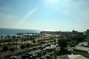A coastal cityscape with a busy street, palm trees, and a view of the sea. - Mediterraneo Suisse (Civitavecchia)