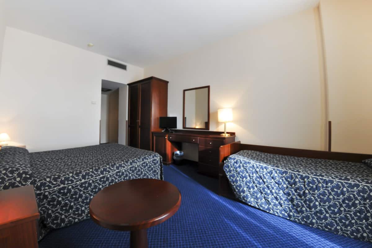 A hotel room with two single beds, a desk, a chair, and a small table.