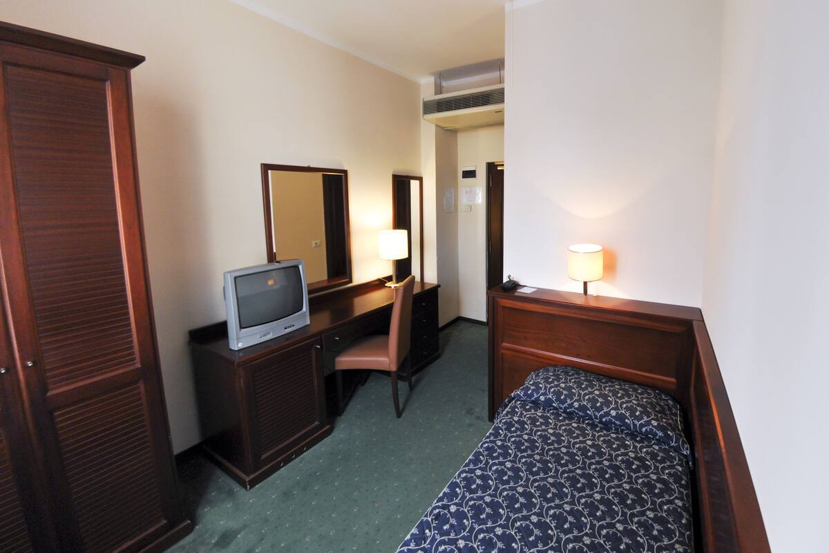 A hotel room with a bed, a desk with a television, a chair, a dresser, and a mirror.