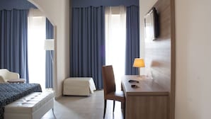 A hotel room with a bed, a desk, a chair, a TV, and curtains.