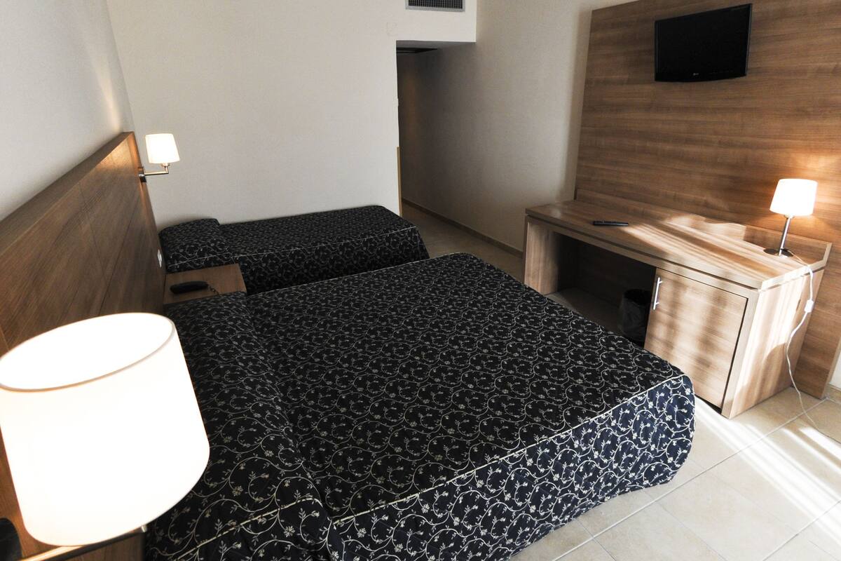A hotel room with a bed, bedside table, lamp, and a TV mounted on the wall.