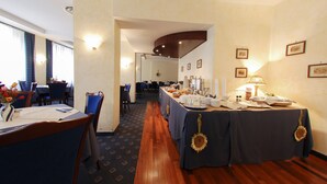 A hotel dining area with tables set for a meal, a buffet line, and a view of the dining area in the background.