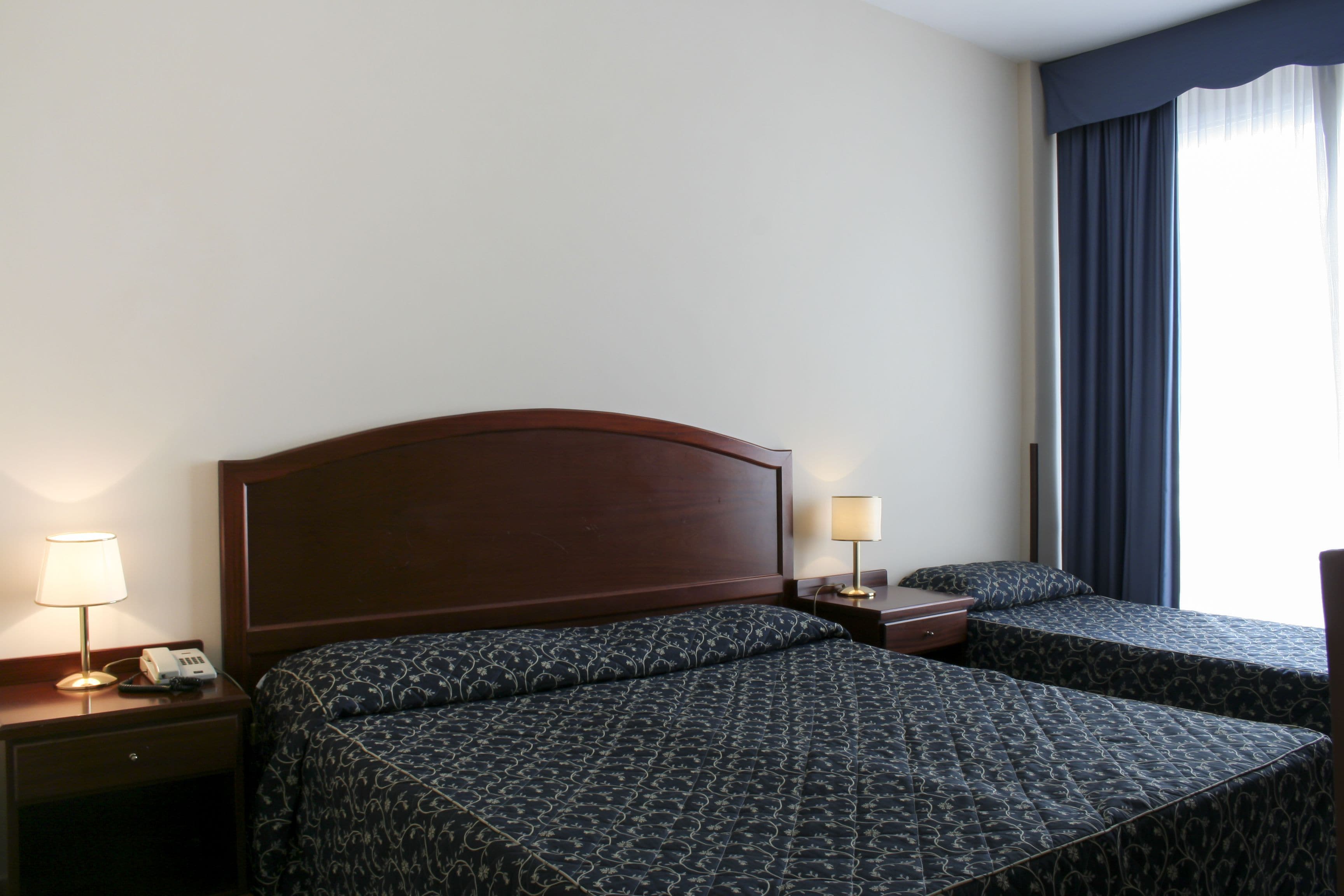 Una habitación de hotel con una cama grande, dos mesitas de noche y un ventanal con cortinas.