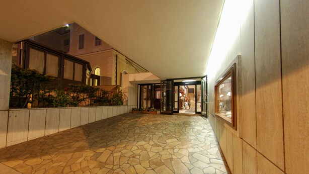 A stone-tiled corridor with a glass door entrance, a potted plant, and a framed picture on the wall.