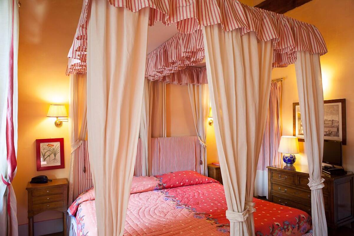A bedroom with a four-poster bed, a bedside table, a lamp, and a framed picture on the wall.