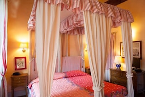 Un dormitorio con una cama con dosel, una mesita de noche, una lámpara y un cuadro en la pared.