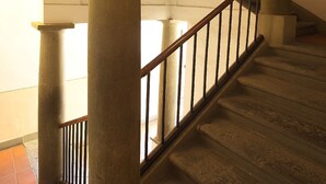Eine Treppe mit Holzhandlauf und Metallspindeln, begleitet von großen Steinpfeilern, die zu einer oberen Ebene führen.