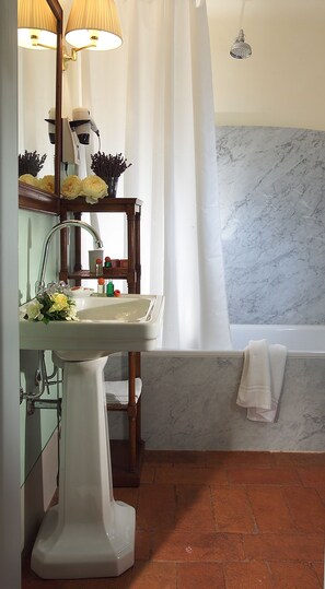 A bathroom with a marble wall, a white sink, a wooden vanity, a mirror, and a shower curtain. - Antica Dimora Firenze  (Florence)