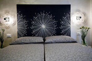 A bed with a patterned bedspread, a black wall with white decorative elements, and two wall sconces. - Domus Diana (Rome)