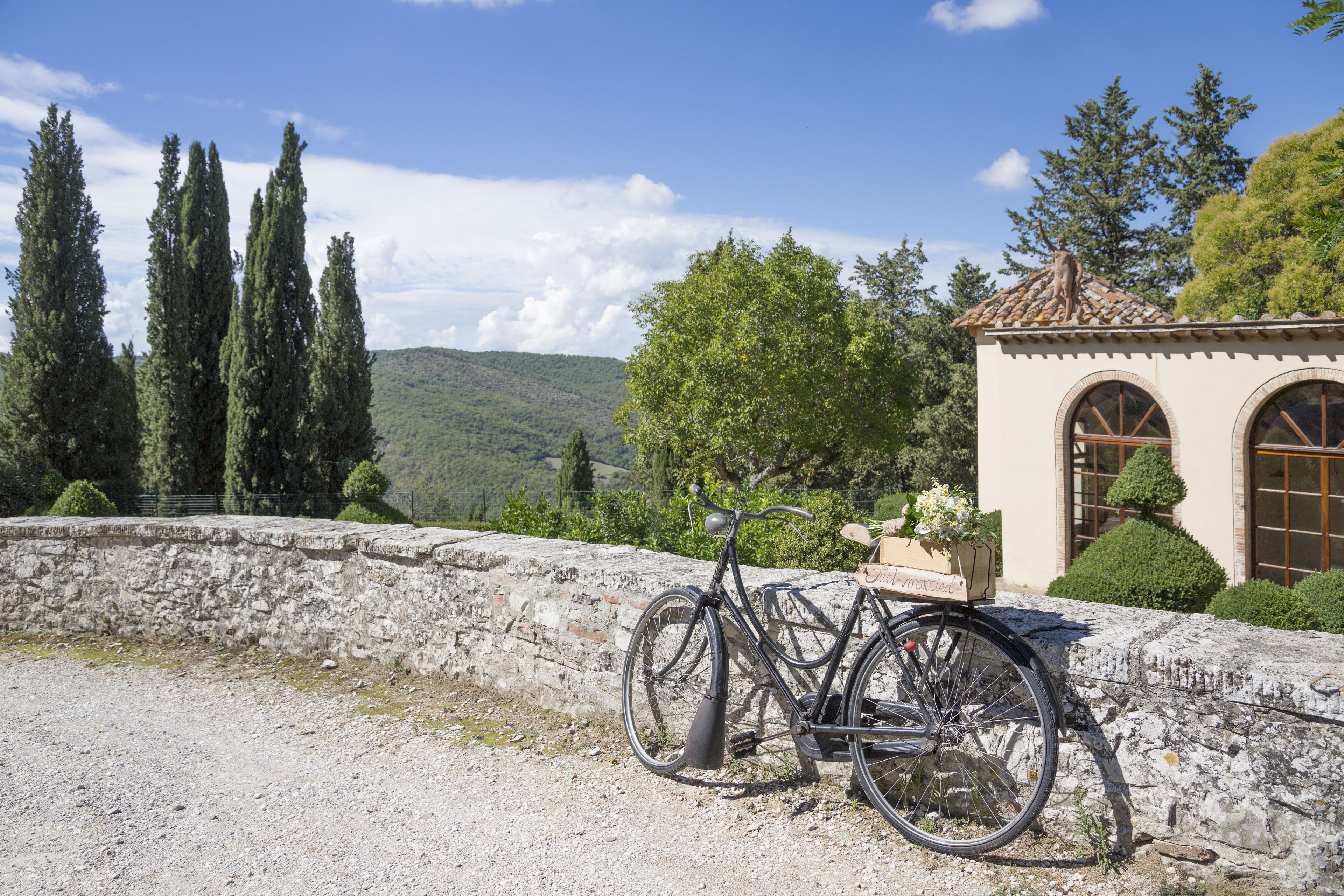 A bicycle parked by a stone wall with a view of a building and trees.