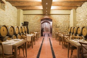 Une cave à vin avec des rangées de barriques en bois, des tables dressées pour le repas et des murs en pierre.