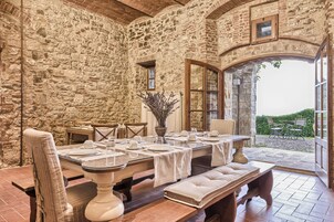 Un'area pranzo con pareti in pietra, un tavolo apparecchiato per quattro persone, una panca e vista all'esterno attraverso un'apertura.