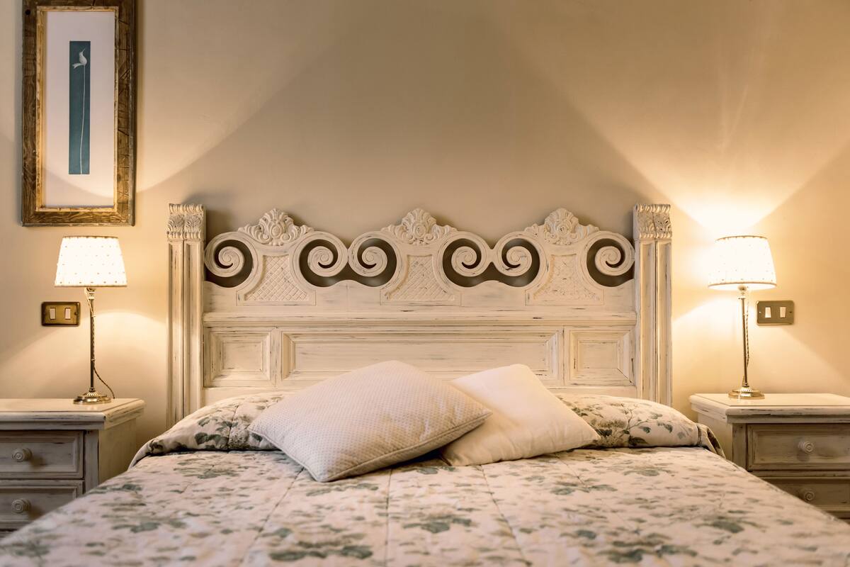 A bedroom with a classic headboard, two bedside lamps, a floral bedspread, and a framed picture on the wall.