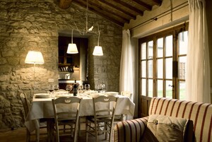 Zona pranzo con parete in pietra, travi in legno e tavolo imbandito per quattro, con calici e piatti.