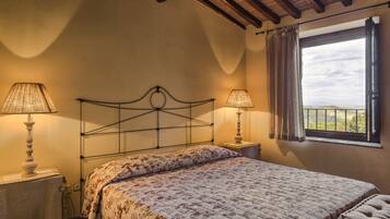 A bedroom with a bed, two bedside lamps, a window with curtains, and a view of the countryside.