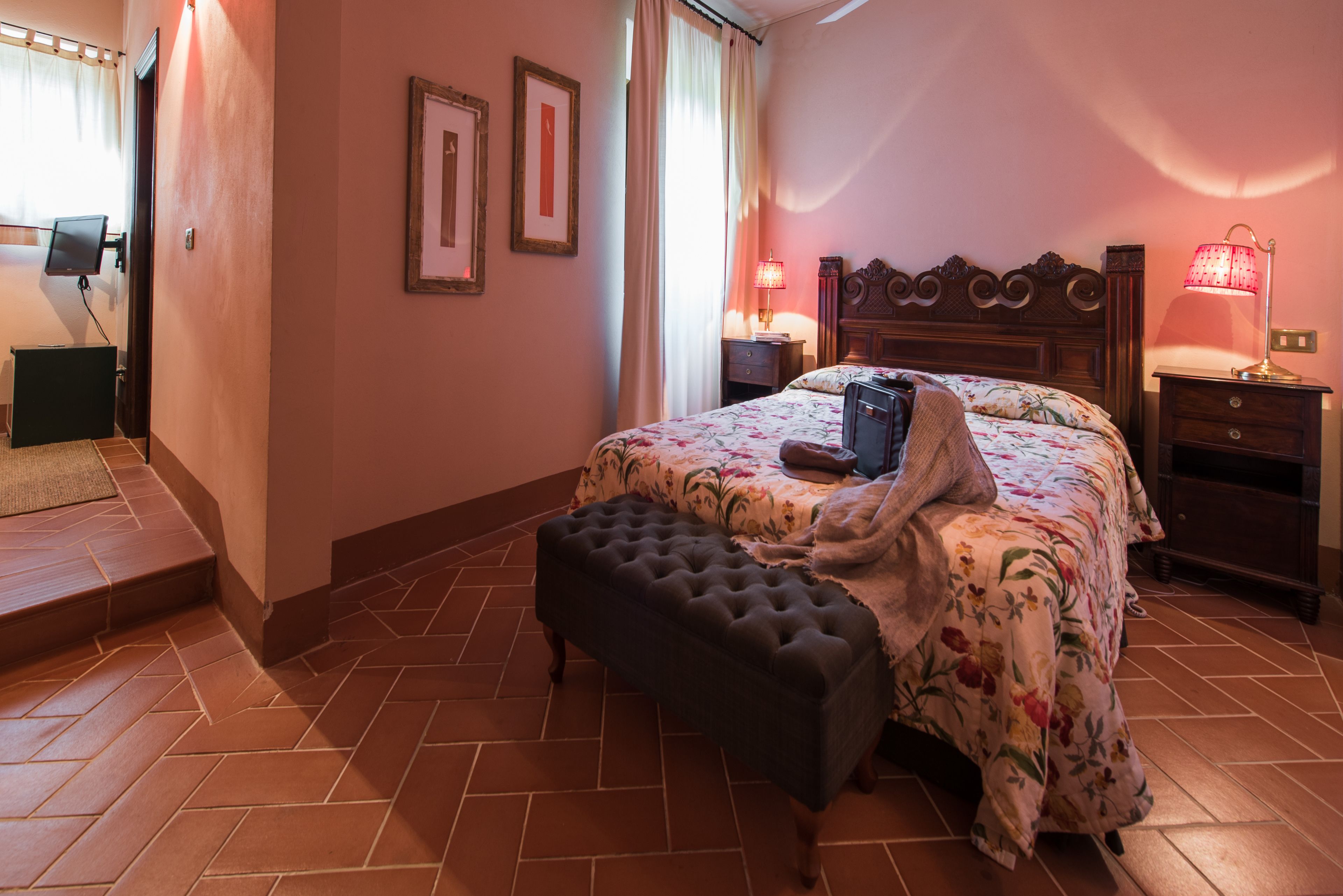Un dormitorio con cama, mesita de noche, lámpara, banco y una puerta.