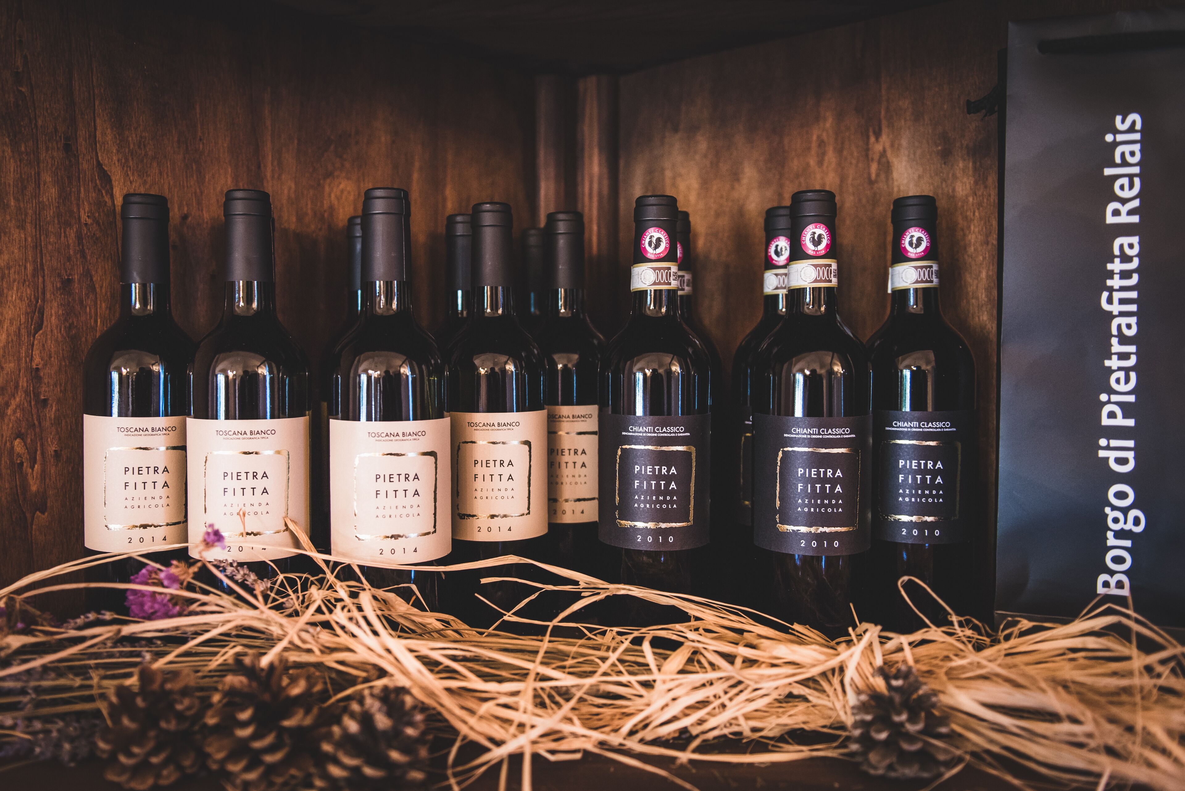 A collection of wine bottles with labels indicating 'Pietra Fitta' and 'Toscana Bianco' on a wooden shelf.