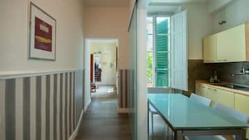 A hallway leading to a dining area with a glass table and chairs, a kitchen with cabinets, and a framed picture on the wall.