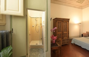 A hotel bathroom with a shower, a wooden cabinet, and a bed. - Casa Rovai Guest House (Florence)
