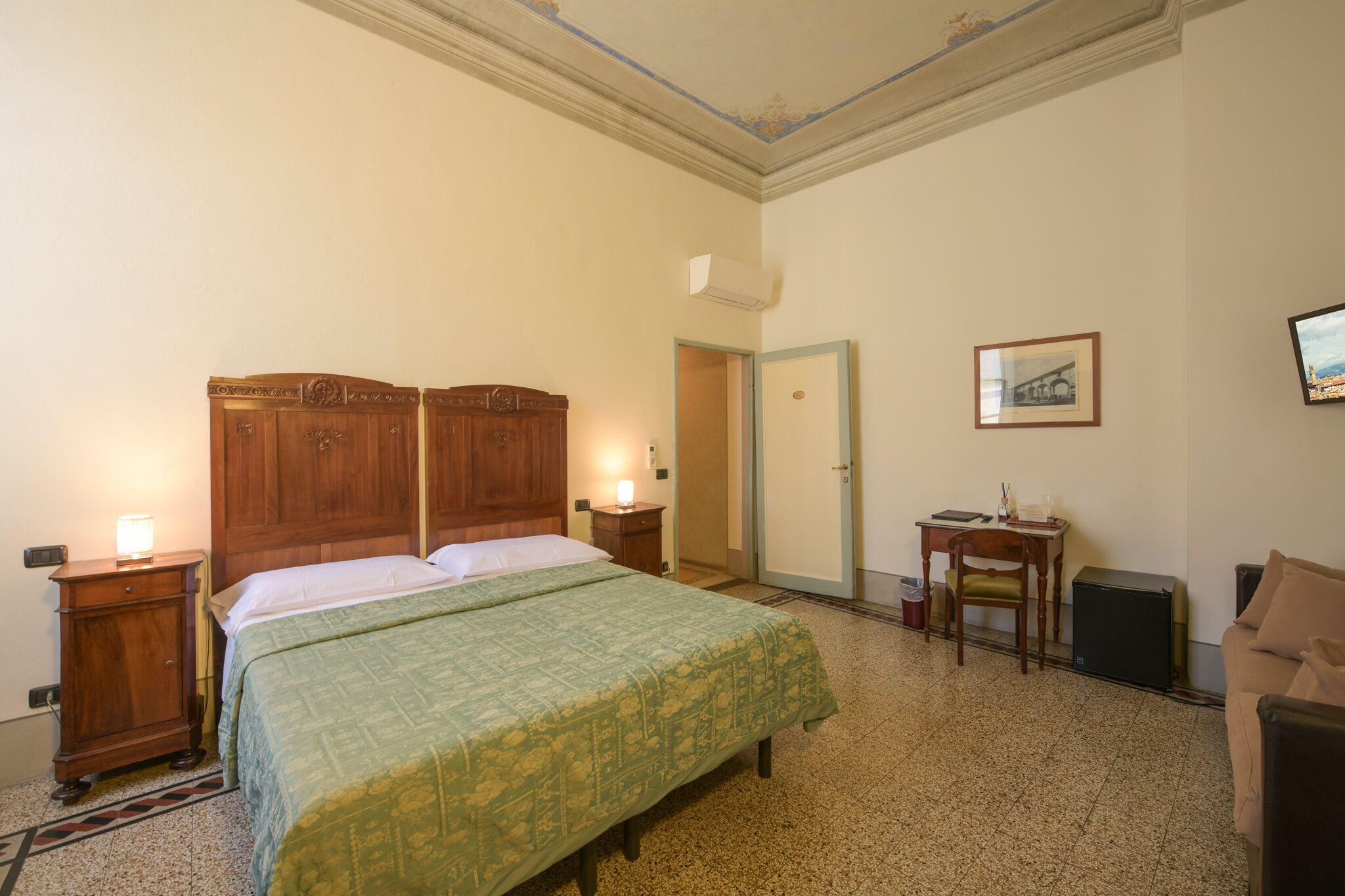 Habitación de hotel con cama doble, escritorio con silla, una mesita y un cuadro en la pared.