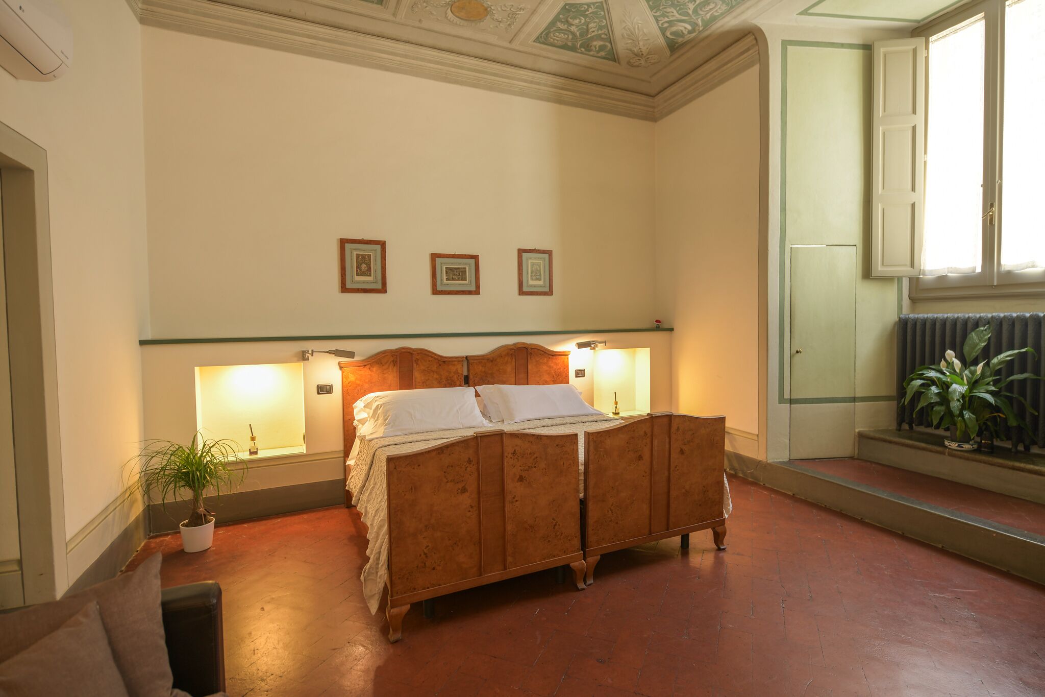 Un dormitorio con una cama de madera, dos lámparas de noche, un radiador y una planta en maceta.