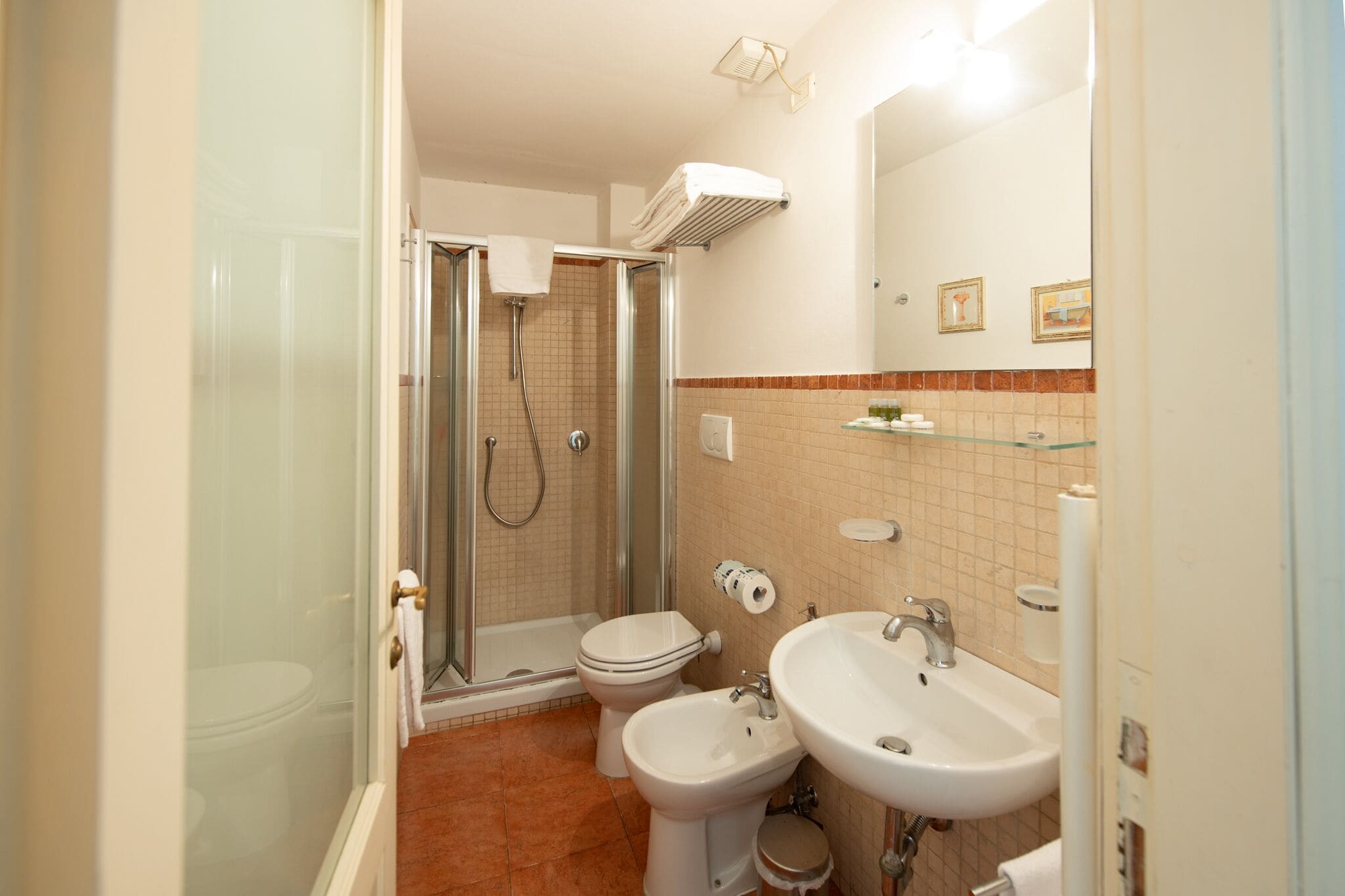 Ein Badezimmer mit Duschkabine, zwei Toiletten, einem Waschbecken und einem Spiegel.