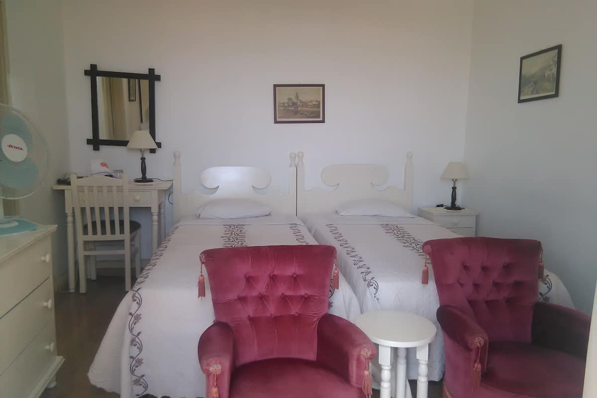 A hotel room with two beds, a desk, a chair, a small table, and a mirror.