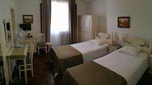 A hotel room with two beds, a desk with a chair, a wardrobe, a television, and a window with curtains. - Pensão Residencial Vila Teresinha (Funchal)