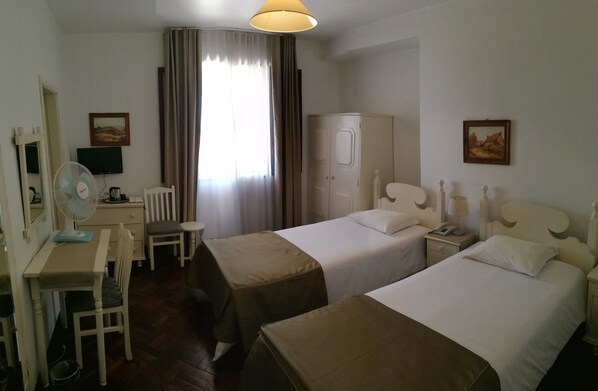 A hotel room with two beds, a desk with a chair, a wardrobe, a television, and a window with curtains.
