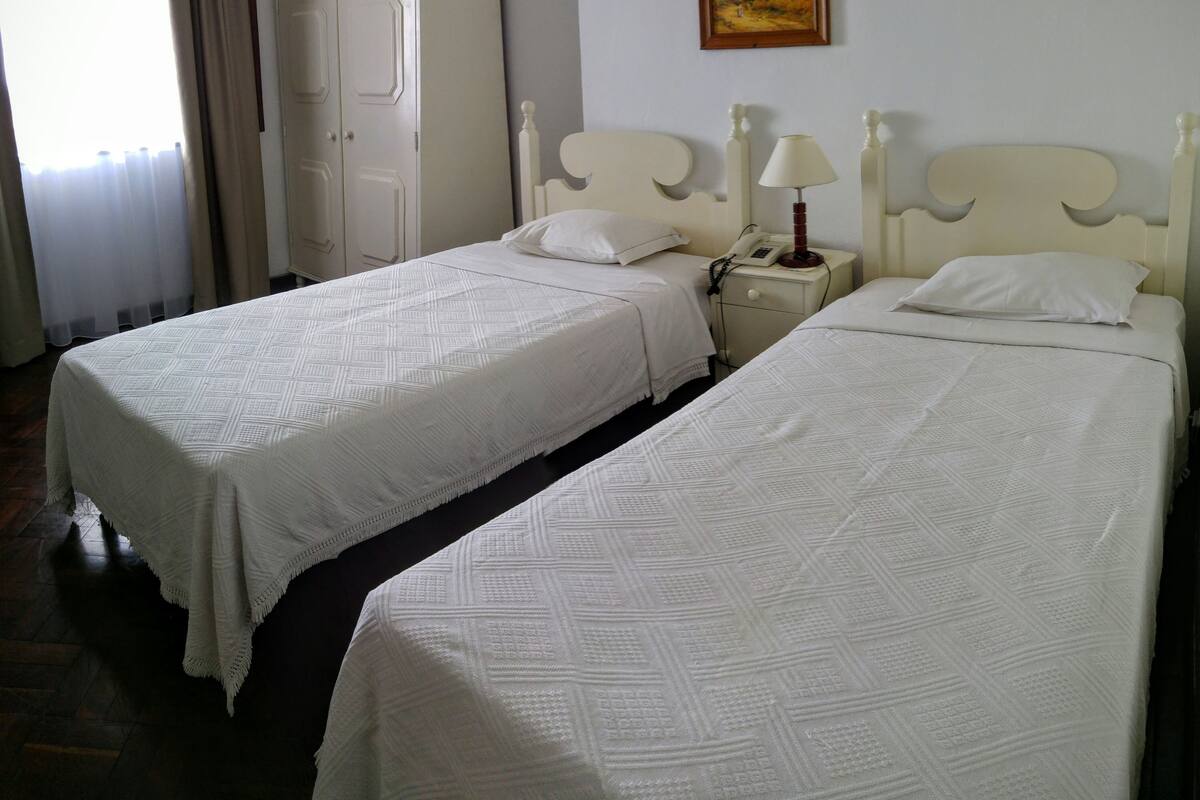 A hotel room with two beds, a wardrobe, a nightstand with a lamp, and a painting on the wall.